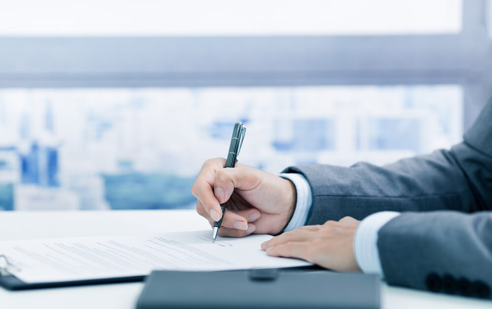Une personne en costume signe un document sur un bureau